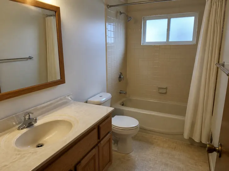 A dated bathroom with an almond-tile tub and shower