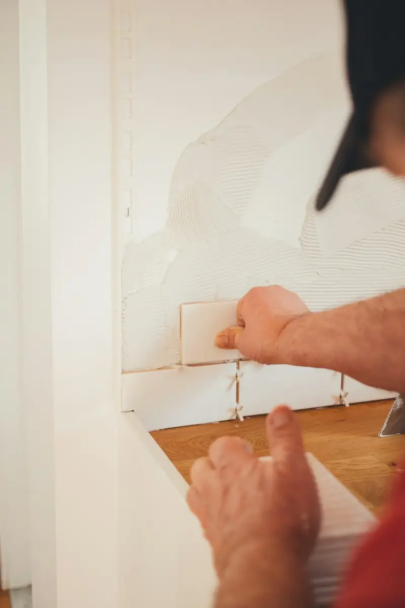 Hands setting a white tile into fresh thinset
